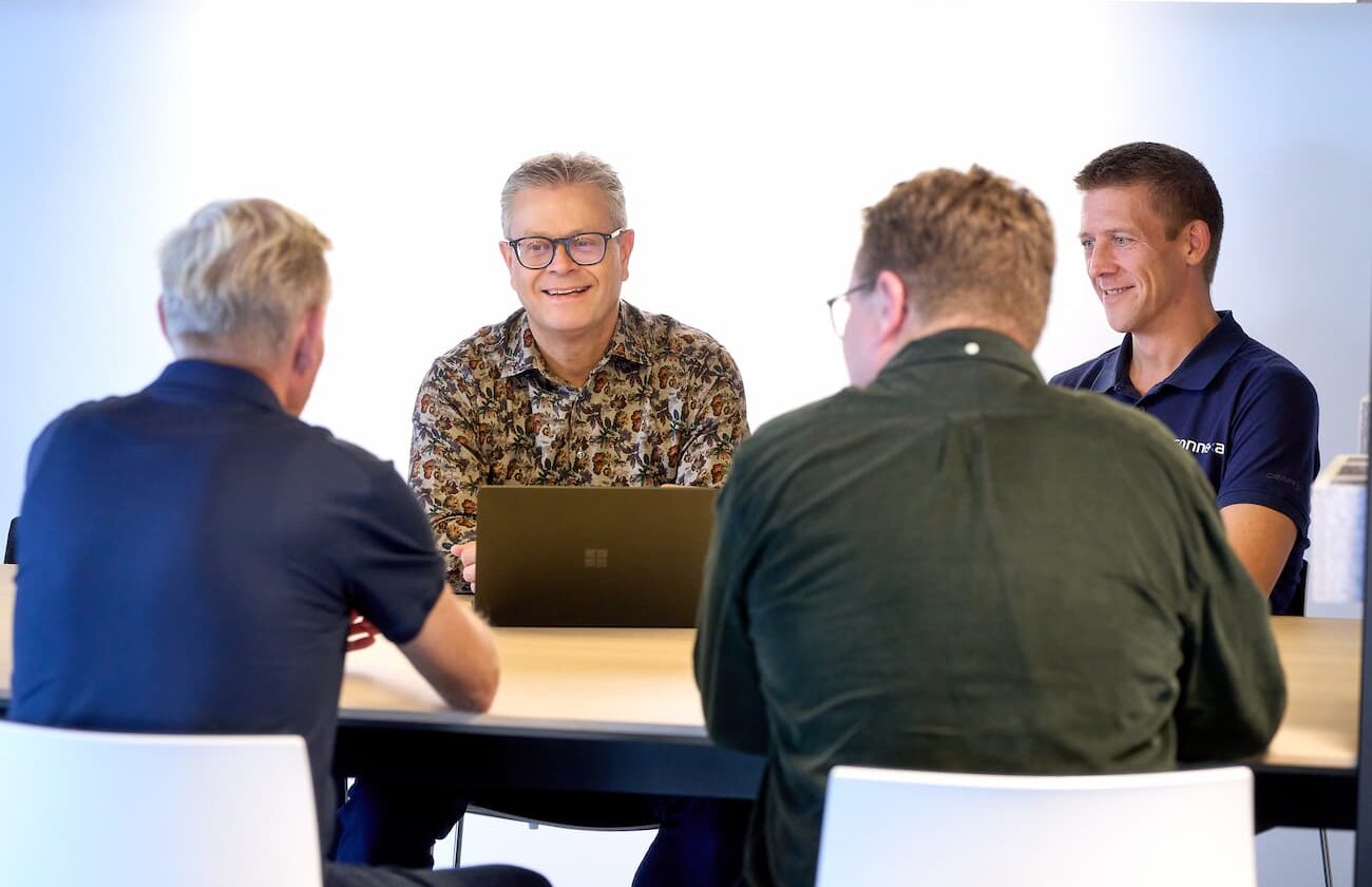 Fire Connexa-medarbejdere sidder i et møderum og arbejder på en fælles opgave. De arbejder med it-support, netværk og sikkerhed for virksomheder